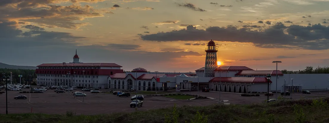 Photographie : le bloc de l'hôtel, les ailes du casino aux toits rouges et la tour en forme de phare du Casino Nouveau-Brunswick au coucher du soleil, vus de l'autre côté du stationnement.